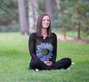 A woman with brown hair sitting cross-legged in a park
