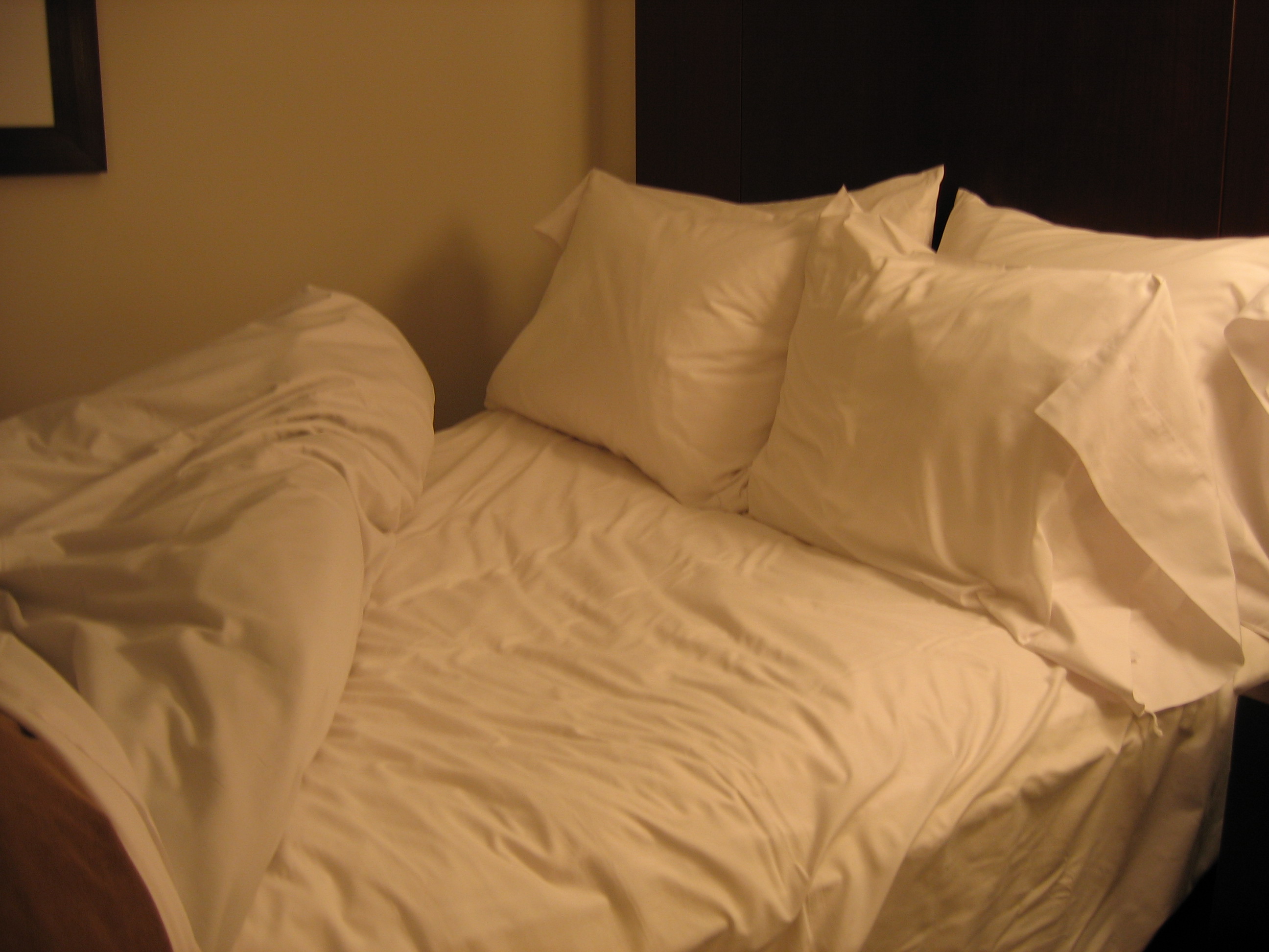 A bed with the covers drawn back revealing white sheets and four pillows