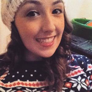woman with curly brown hair wearing a sweater and beanie
