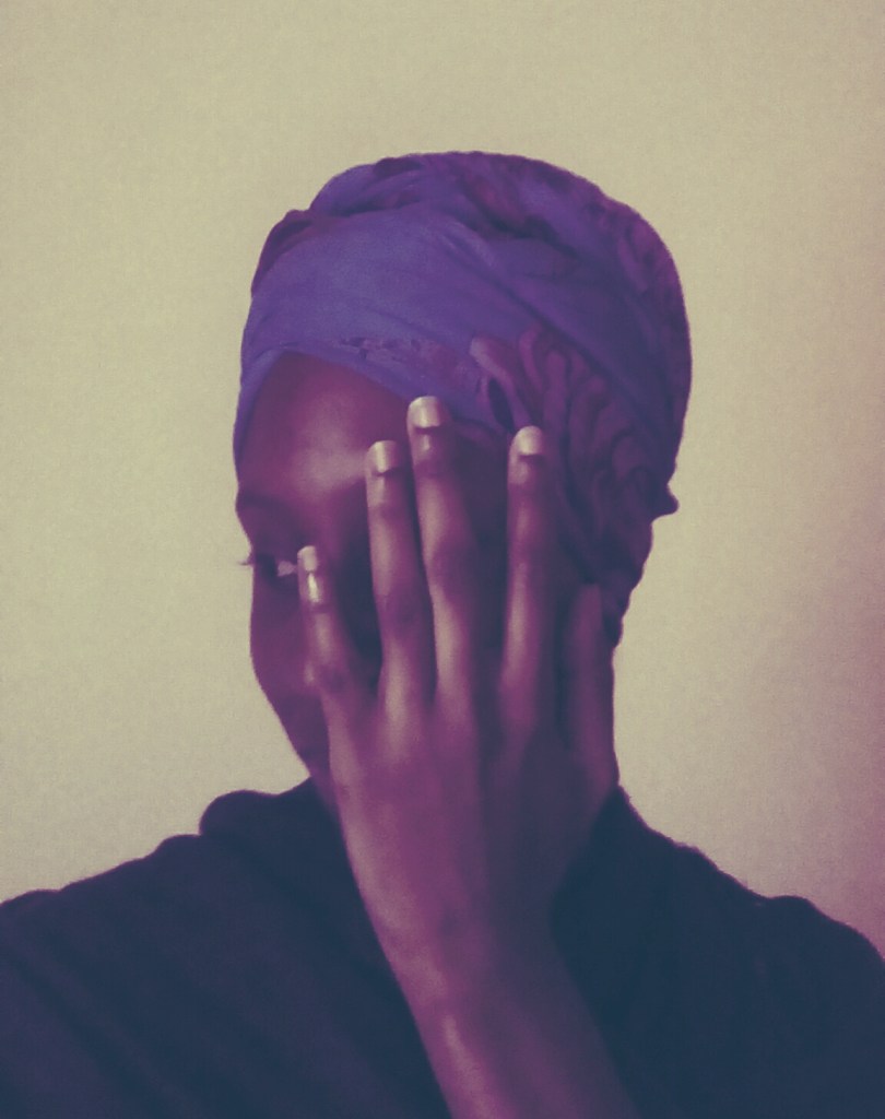 African American woman wearing a purple wrap around her head decorated with pink flowers