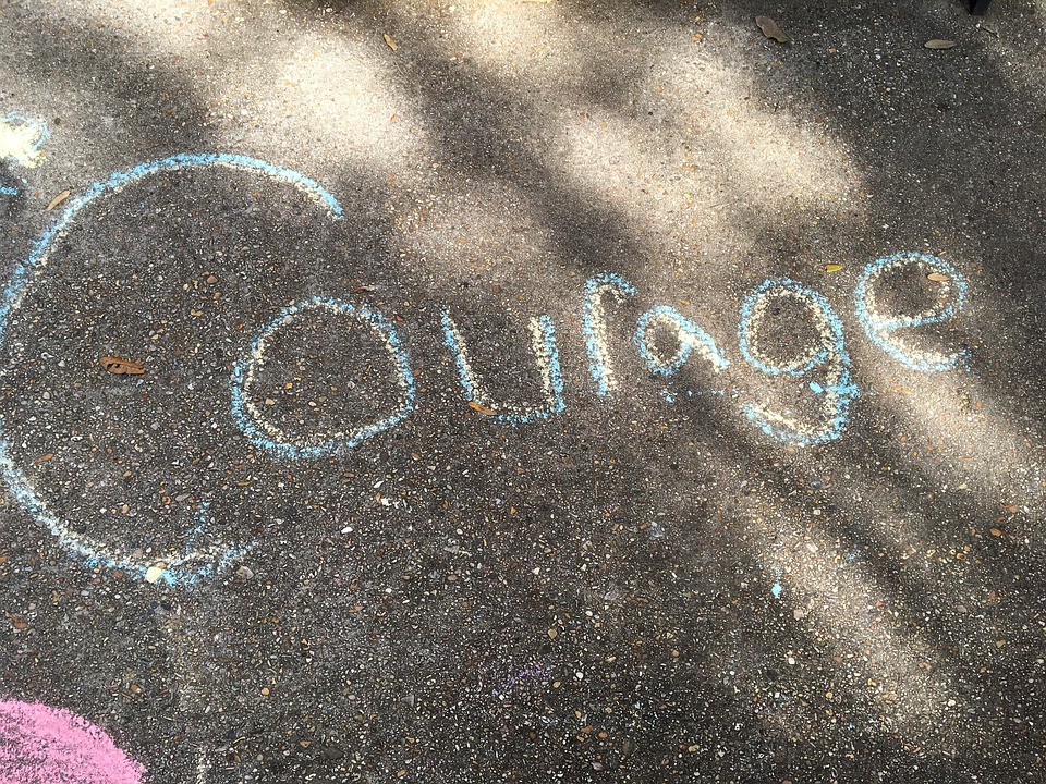 The word "courage" written with blue and yellow chalk on an asphalt road 
