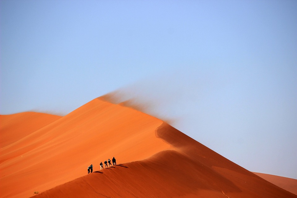 People walking on a sand dune in a vast desert