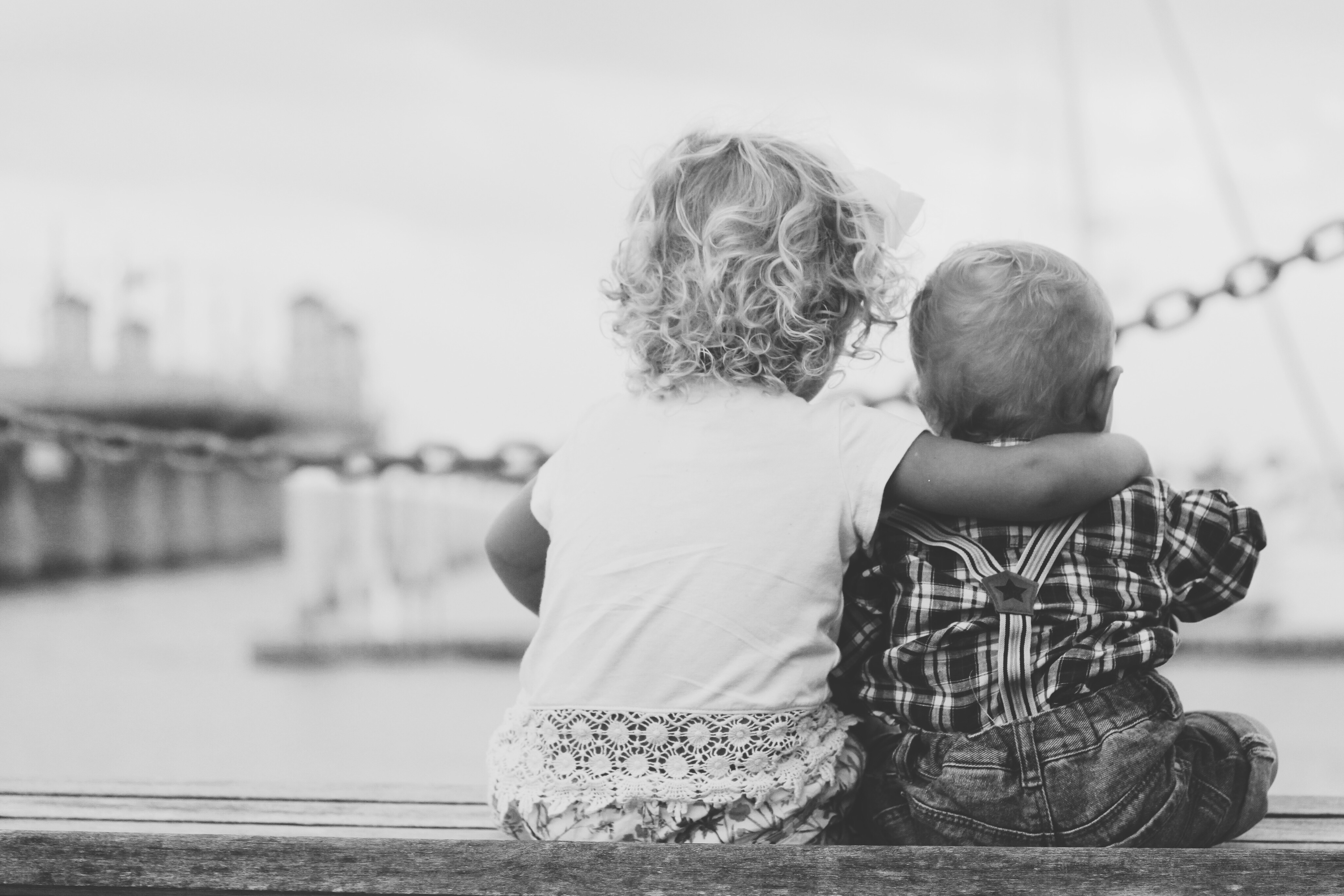Two toddlers sitting next to each other overlooking an ocean pier