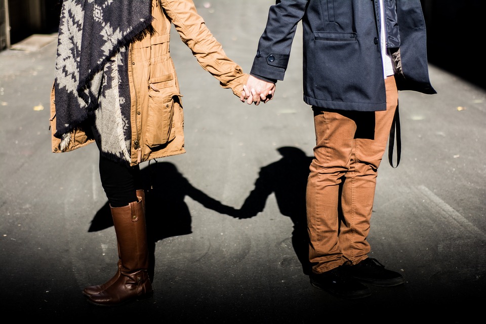 Two people holding hands while walking down a street