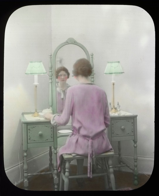 Vintage photograph of woman wearing pink bathrobe and sitting in front of a vanity mirror