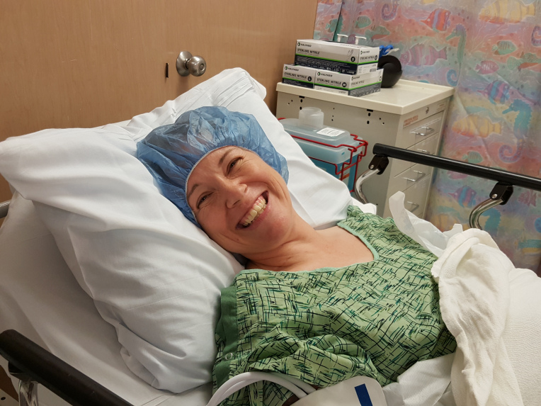 Photo of Lisa before June 30 2014 surgery; wearing hospital gown and cap lying in bed