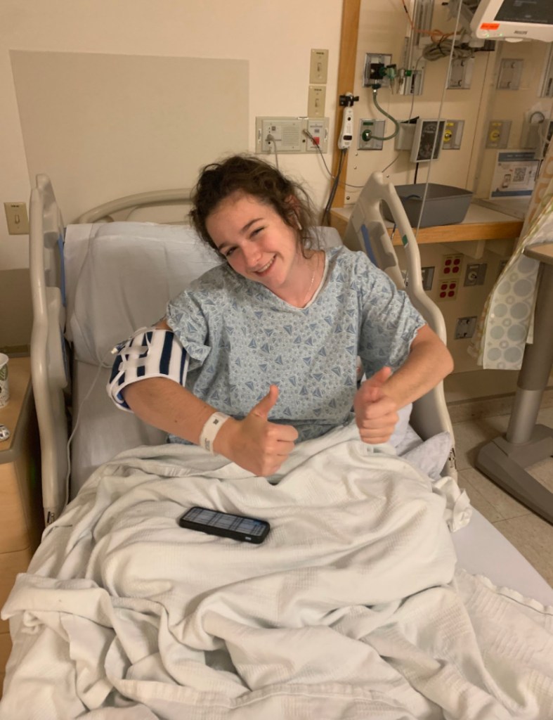 Young woman in hospital bed giving two thumbs up and smiling