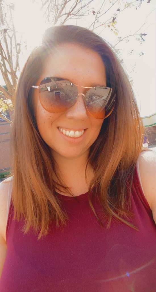 Woman with auburn hair wearing sunglasses and a burgundy tank top