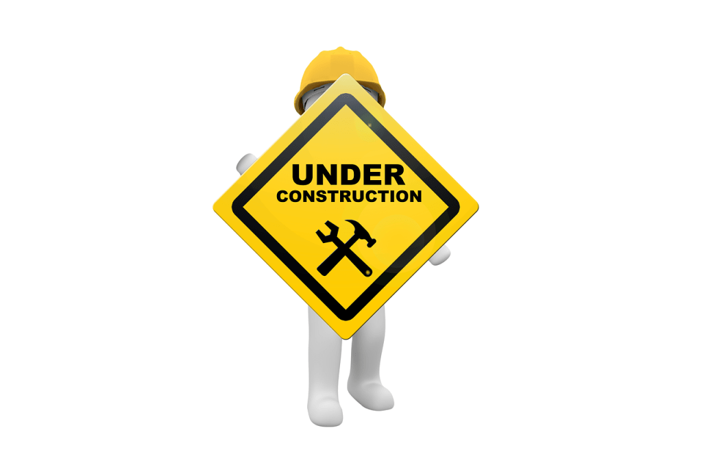 A man wearing a yellow hardhat holding an "Under Construction" sign 