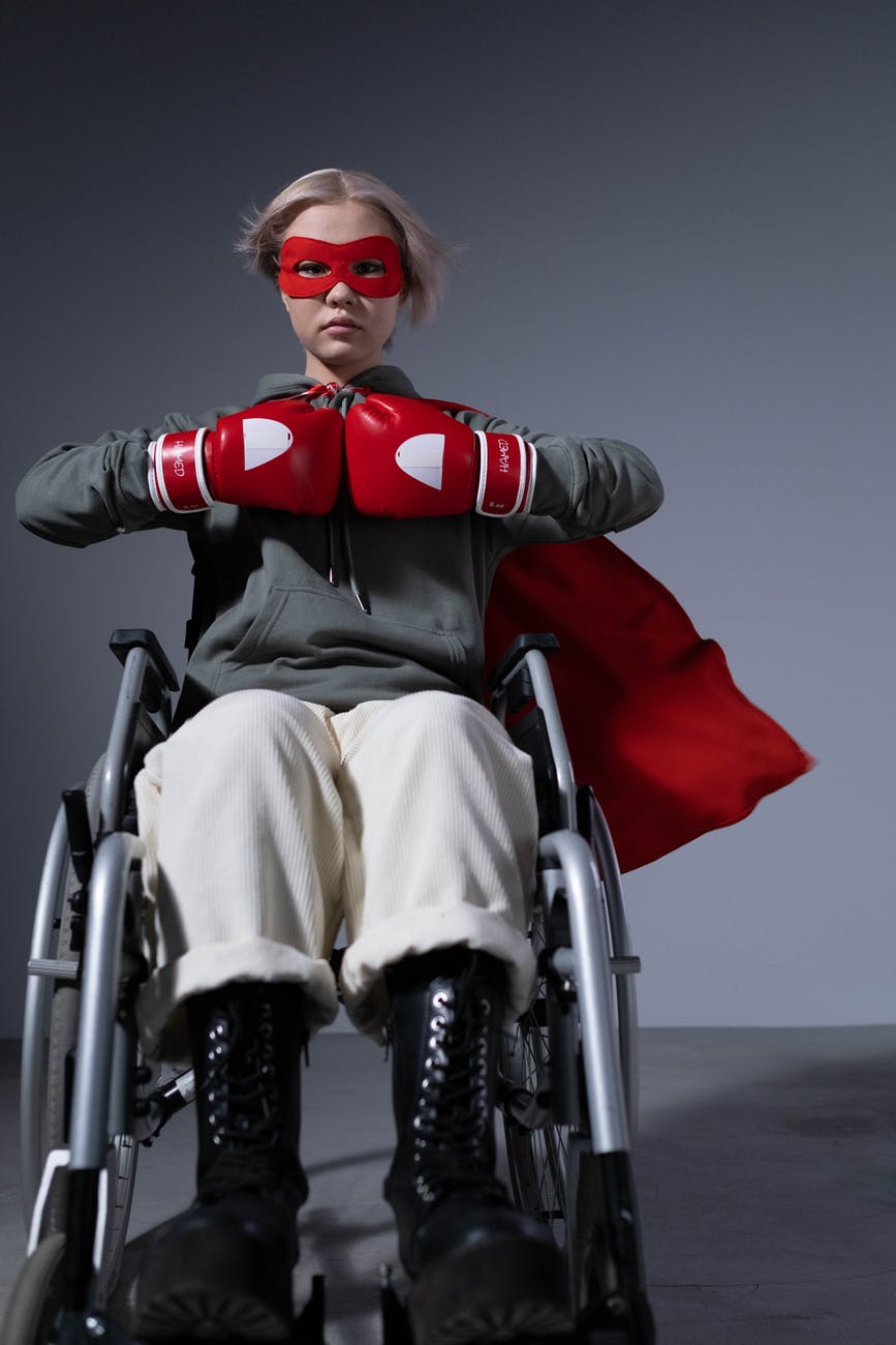 young woman in wheelchair wearing a superhero mask, a cape, and boxing gloves. Badass.
