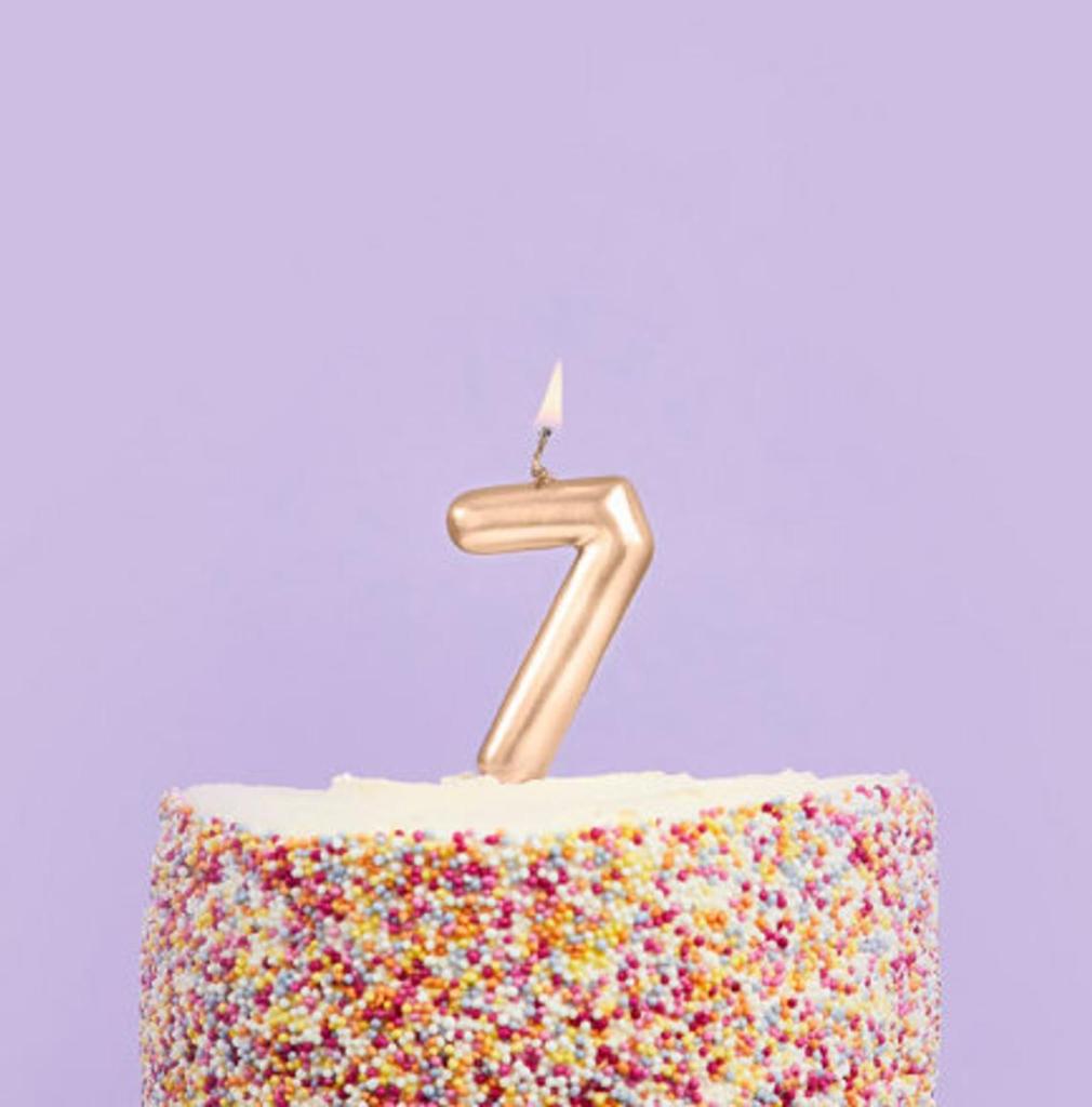 Candle shaped like the number 7 burning atop a sprinkled cake