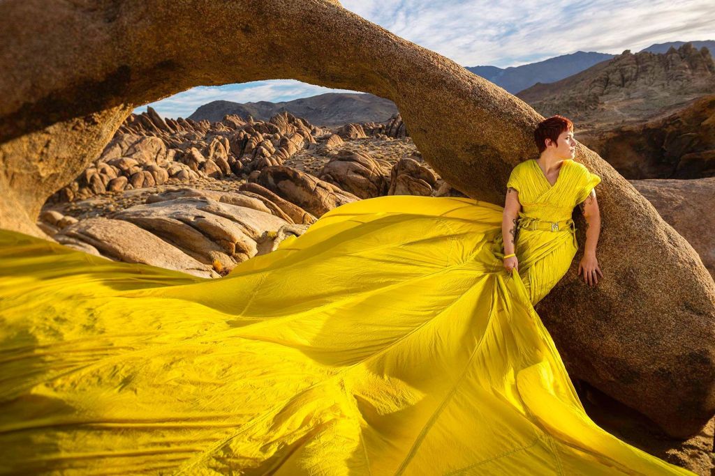 woman in a long yellow gown standing against a rock arch near Lone Pine, CA